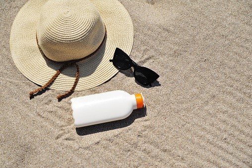 hat, shades, and sunscreen on a beach.